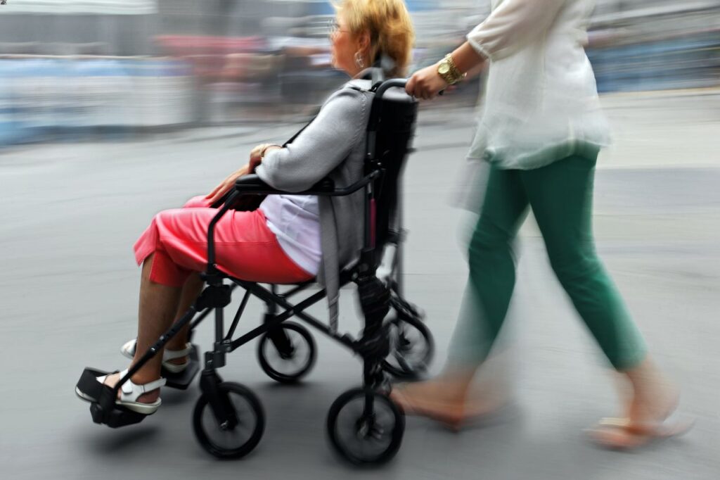 A woman pushes a wheelchair a disabled senior sits in