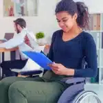 Woman in wheelchair holding clipboard and documents. Disabled Adult Child (DAC) Benefits